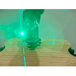 Ein Kreuzlinienlaser mit grünem Licht steht auf einer Holzplatte.