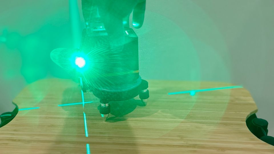 Ein Kreuzlinienlaser mit grünem Licht steht auf einer Holzplatte.