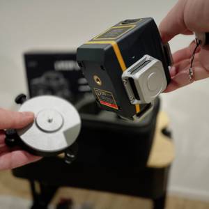 Der Cigman-Kreuzlinienlaser und sein Stativ werden hochgehalten.