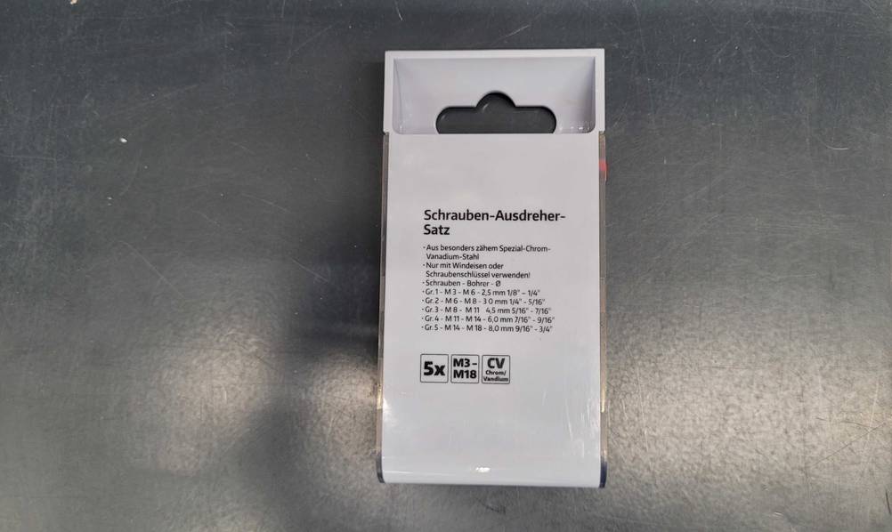Rückseite einer Packung der getesteten Schraubenausdreher mit Inhaltsangabe auf einer Metallfläche.