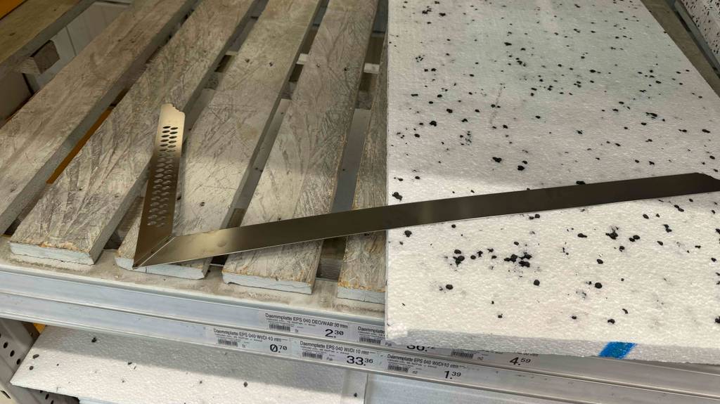 Ein Zimmermannswinkel liegt zum Testen halb auf einem Holzlattenregal und halb auf einer Styroporplatte.