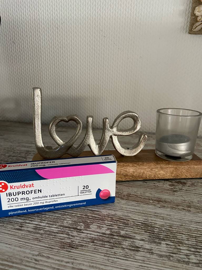 Getestet: Das Kopfschmerzmittel in der Packung mit zwanzig Ibuprofen-Tabletten liegt vor einem Kerzenständer auf einem Holztisch.