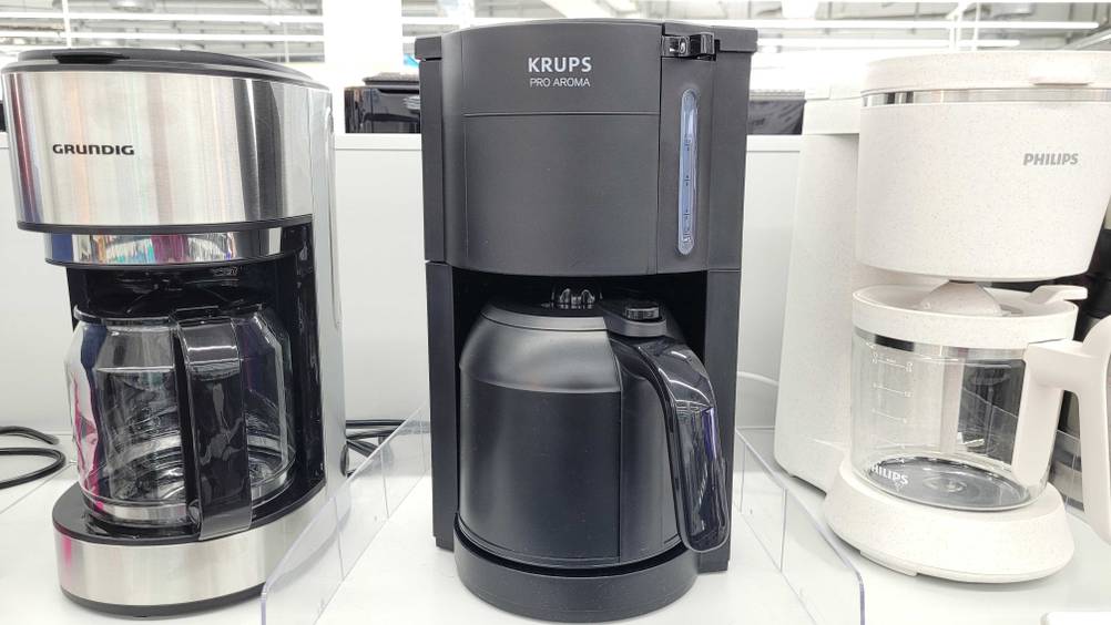 Eine getestete Krups-Kaffeemaschine zwischen anderen auf einem Regal.