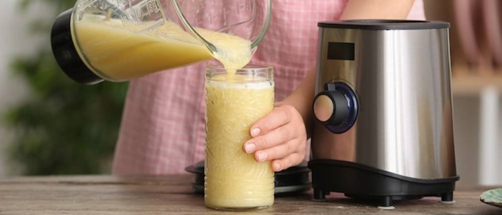 Standmixer von Krups im Test: Eine Frau füllt einen gelben Smoothie aus einem Standmixer-Behälter in ein großes Glas.