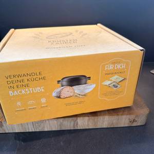 Der Karton vom Krustenzauber-Gusseisen-Topf steht auf einem Holzbrett