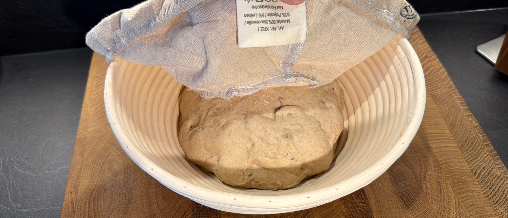 Eine Hand entfernt den Stoff von der Bambusschale vom Krustenzauber-Gusseisen-Topf