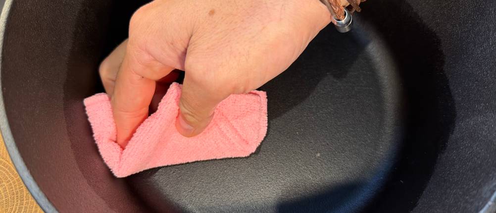 Eine Hand wischt mit einem Lappen durch den Krustenzauber-Gusseisen-Topf