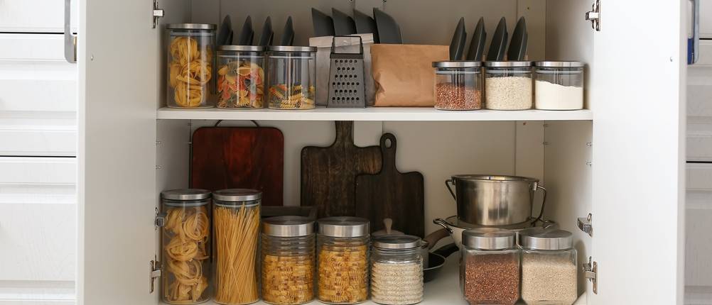 Glasbehälter mit Nudeln und Reis stehen in einem gut sortierten Unterschrank.