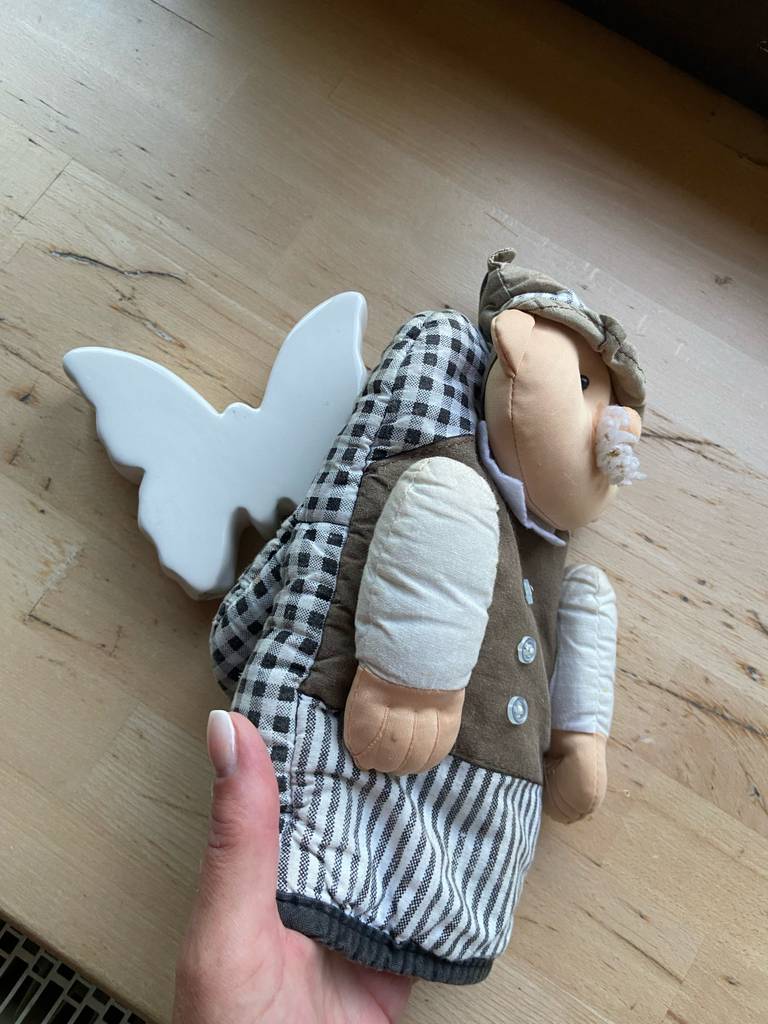 Eine Hand hält den getesteten Küchenhandschuh aus schwarz-weiß kariertem Stoff mit darauf befestigter Puppe über einem Holztisch.