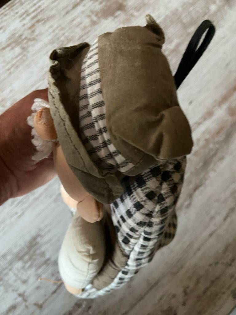 Eine Hand hält den getesteten Küchenhandschuh in schwarz-weißem Karomuster mit darauf genähter Puppe über einer Holzoberfläche.