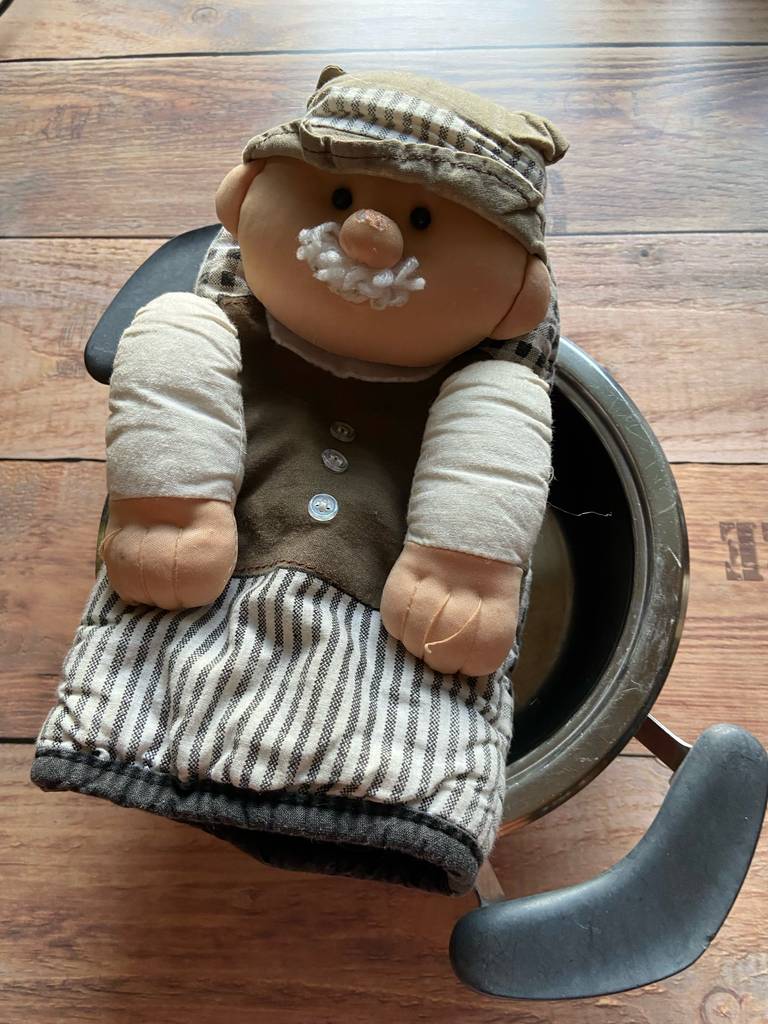 Küchenhandschuhe-Test: Ein schwarz-weiß karierter Handschuh, darauf ist eine ausgestopfte Puppe mit Bart genäht, liegt auf einem Topf.