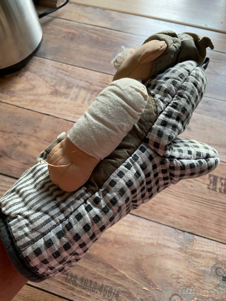 Küchenhandschuhe im Test: Ein schwarz-weiß karierter Handschuh, darauf ist eine ausgestopfte Puppe genäht, ist über einer Hand.