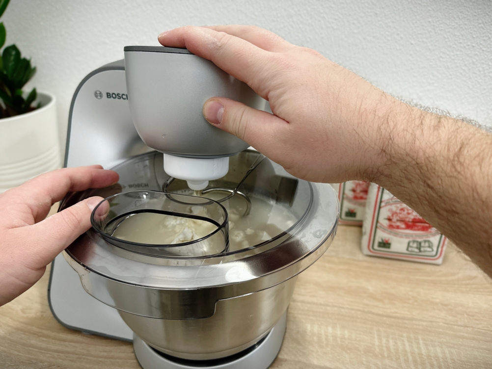 Hefemischung wird in die bereits gemischte Teigmasse in der Bosch MUM56340 gegeben. Der Knethaken ist in Betrieb.