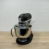 Die KitchenAid Artisan steht vollständig montiert auf einer Holzplatte. Die Schüssel ist eingesetzt, der Spritzschutz montiert.