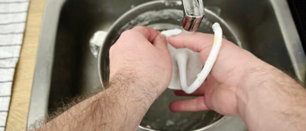 Der Teighaken der Küchenmaschine KitchenAid Artisan wird unter fließendem Wasser von Hand gereinigt. Die Spüle besteht aus Edelstahl.