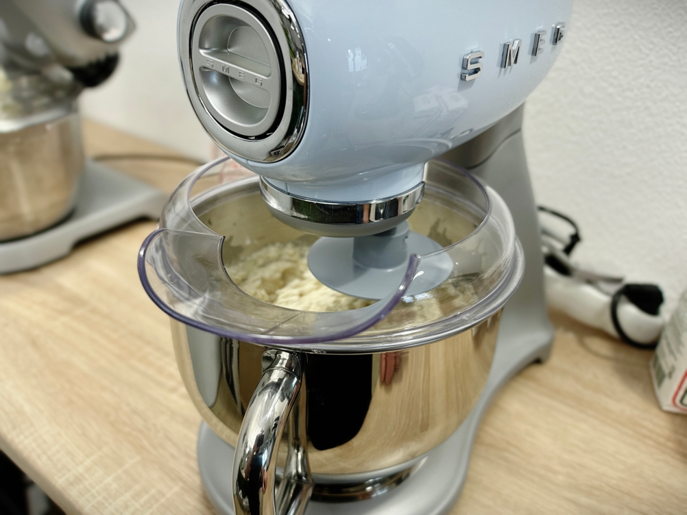 Die Küchenmaschine Smeg SMF02PBEU knetet gerade einen Teig in der Edelstahlschüssel. Die Rührbewegung ist deutlich sichtbar.