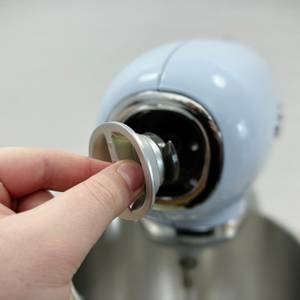 Ein Teil wird in die Frontöffnung der Küchenmaschine Smeg SMF02PBEU eingesetzt. Der Anschluss dient für weiteres Zubehör.
