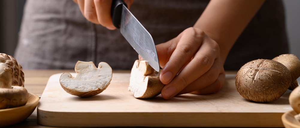 Küchenmesser-Test: Frau schneidet Pilze mit einem Küchenmesser auf einem Holzbrett.