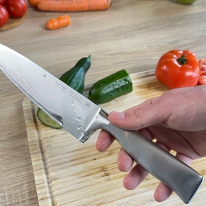 Das WMF-Grand-Gourmet-Messer wird mit feuchten Händen gehalten. Im Hintergrund sind Tomaten, Gurken und Karotten zu sehen.