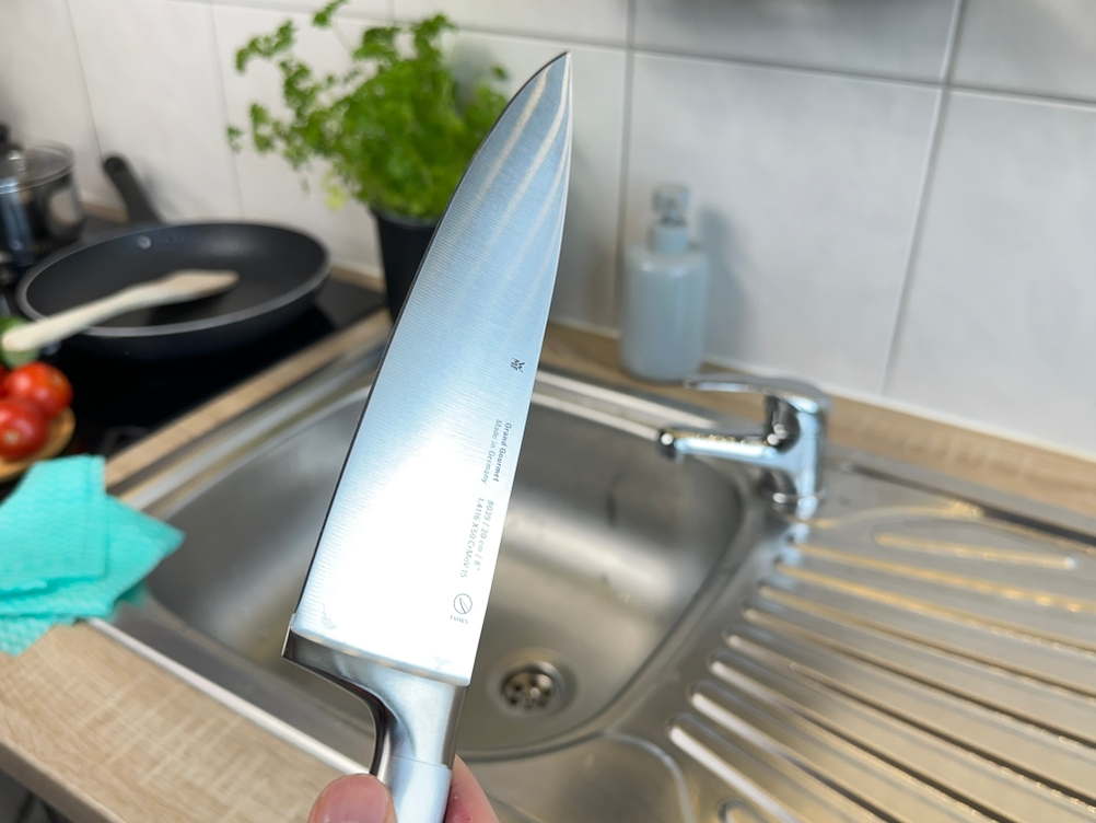Das WMF-Grand-Gourmet-Messer wird frisch gespült über der Küchenspüle gehalten. Die Klinge glänzt im Licht.