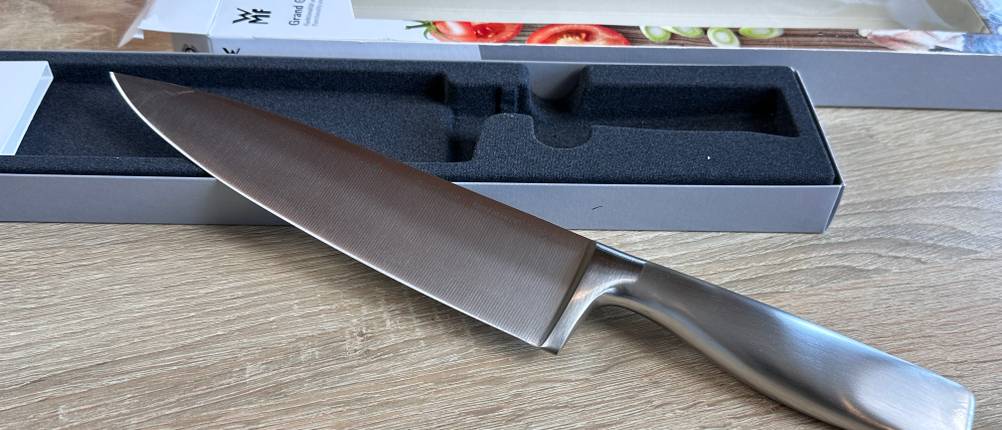 Das WMF-Grand-Gourmet-Messer liegt ausgepackt in einer passgenauen schwarzen Schachtel. Die Verpackung ist geöffnet und daneben platziert.