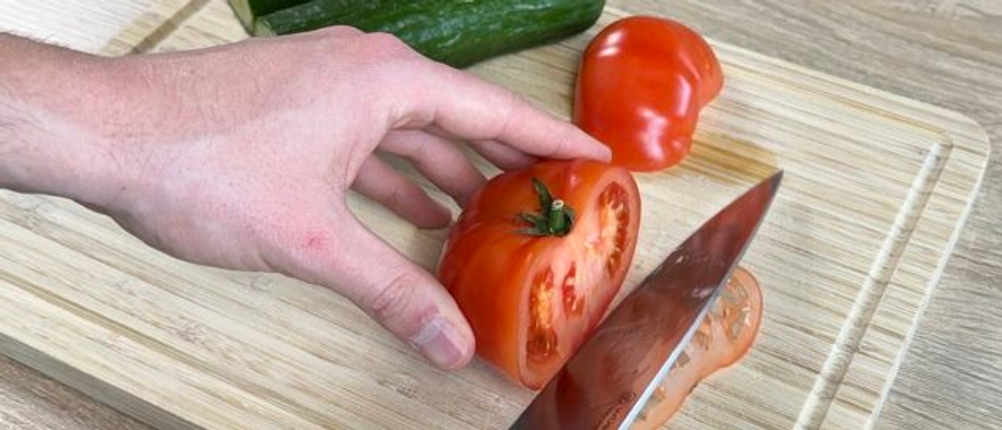 Ein Wüsthof-Chefmesser schneidet eine Tomate auf einem Holzbrett. Die Hand fixiert die Tomate beim Schneiden.