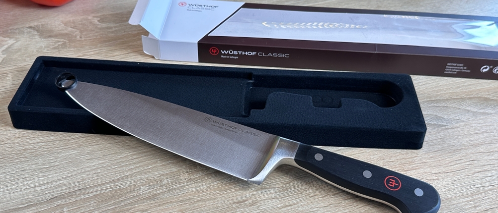 Das Wüsthof-Chefmesser liegt an einer schwarzen Verpackung. Im Hintergrund ist die geöffnete Produktbox zu sehen.