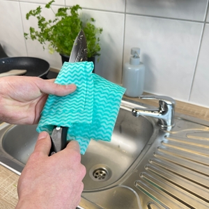 Das Zwilling-1001364-Messer wird mit einem feuchten Schwammtuch in der Nähe der Spüle gereinigt. Reste sind noch auf der Klinge erkennbar.