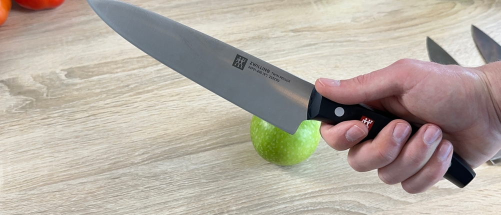 Das Zwilling-1001364-Messer wird in der Hand gehalten. Im Hintergrund liegen Tomaten, Karotten und ein grüner Apfel.
