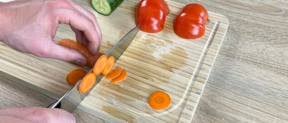 Das Zwilling-1001364-Messer schneidet eine Karotte auf einem Holzbrett. Daneben liegen Gurken und Tomaten.