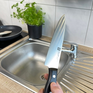 Das Zwilling-1001364-Messer wird nach dem Spülen über der Spüle gehalten. Auf der Klinge sind keine Kräuterreste sichtbar. 