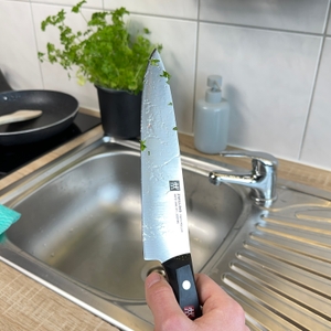 Das Zwilling-1001364-Messer wird mit Kräuterresten in der Hand über das Spülbecken gehalten. Die Klinge ist noch verschmutzt.