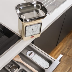 Eine analoge Küchenwaage mit Blech-Behälter steht auf einer Küchen-Arbeitsplatte.