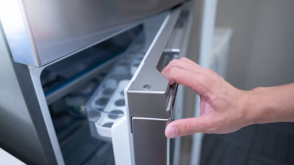 Kühlschrank mit Gefrierfach freistehend im Test: Eine Hand zieht eine Kühlschranktür in silber in einer Griffmulde auf.