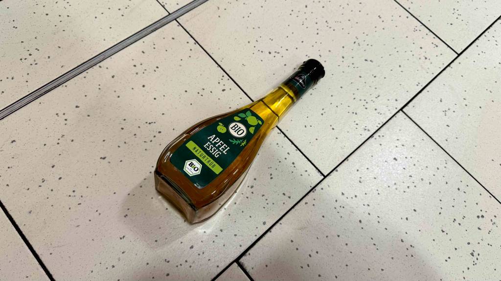 Eine Flasche getesteter Bio-Essig liegt auf einem Fliesenboden.