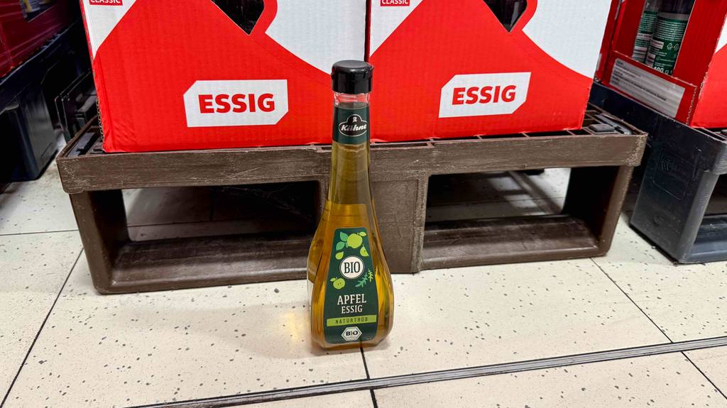 Eine Flasche getesteter Bio-Essig steht vor einer Palette mit Kartons mit der Aufschrift Essig.