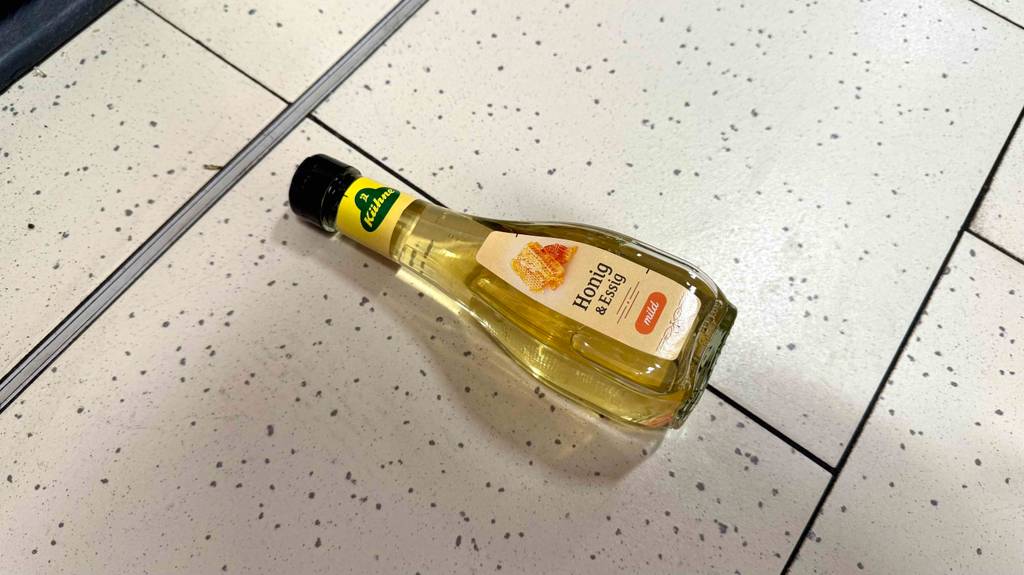 Eine Flasche Honig-Essig liegt getestet auf einem Fliesenboden.