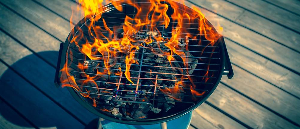 Ein Kugelgrill mit brennender Kohle steht auf einem Steg.