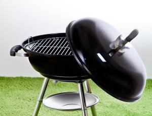 ein Kugelgrill, dessen zur Hälfte auf dem unteren Teil liegt, steht auf einem grünen Untergrund.
