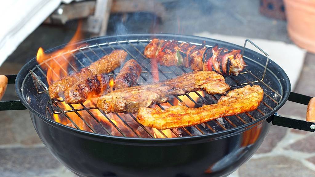 Kugelgrill mit brennenden Kohlen und verschiedenem Grillgut auf dem Grillrost.
