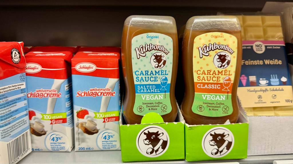 Karamellsosse im Test: Mehrere Flaschen verschiedener Sorten stehen zwischen anderen Produkten in einem Regal.