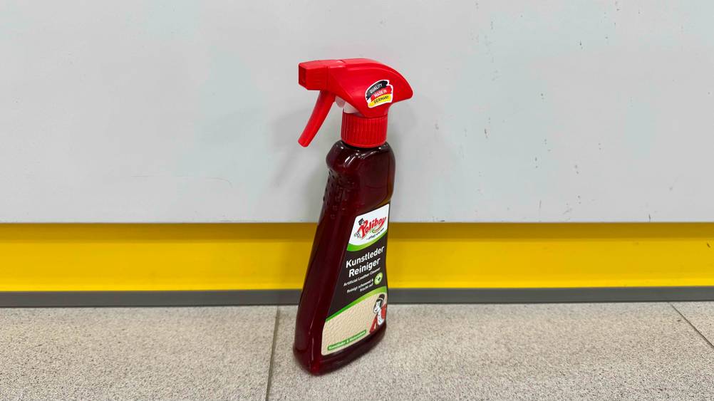 Eine Flasche der getesteten Kunstleder-Pflege steht leicht seitlich vor einem Regal auf dem Boden.