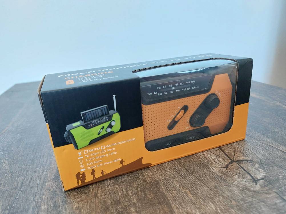 Ein getestetes Kurbelradio in Originalverpackung mit einem transparenten Sichtfenster auf einem Holztisch.