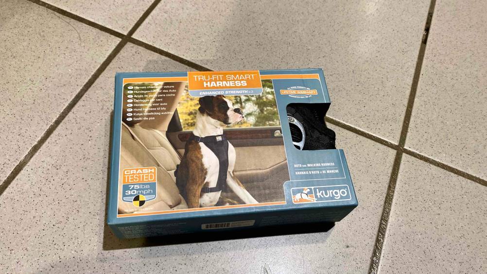 Ein getestetes Sicherheitsgeschirr für den Hund in seiner Originalverpackung mit Sichtfenster auf einem Fließenboden.