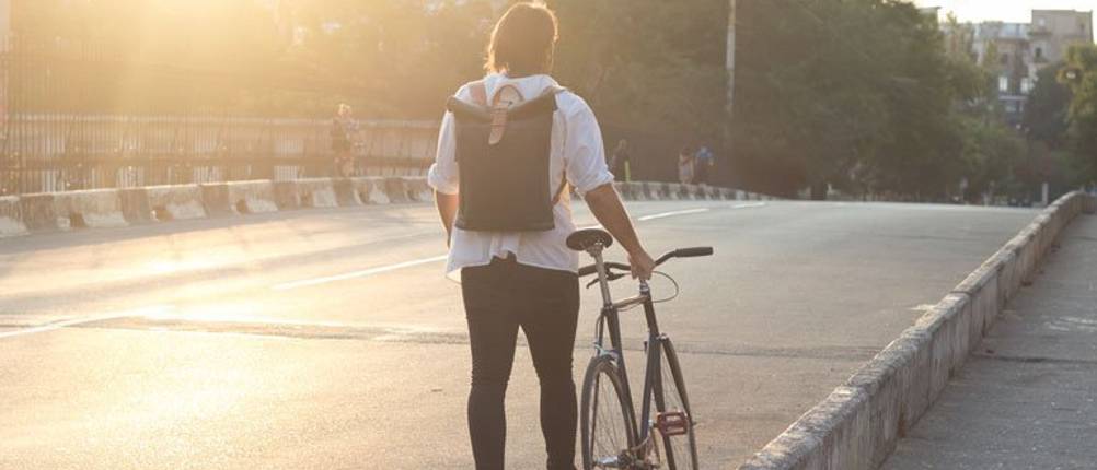 Kurier-Rucksack-Test: Ein Kurier mit schwarzem Rucksack schiebt ein Fahrrad auf einer Straße.