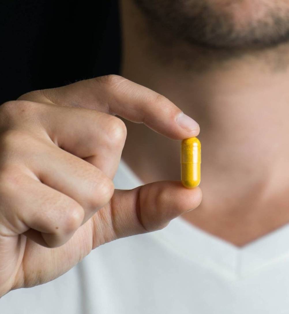 Kurkuma-Kapseln-Test: Ein Mann hält eine gelbe Kurkuma-Kapsel in der Hand. 