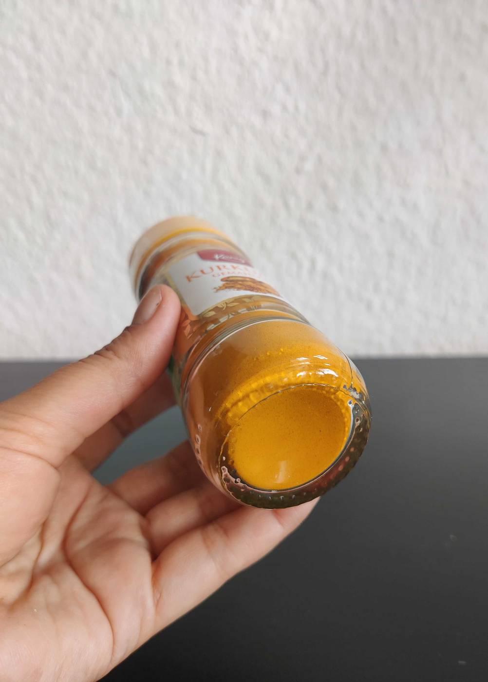 Kurkumapulver getestet: Nahaufnahme des Bodens eines Gewürzstreuers von einer Hand gehalten.