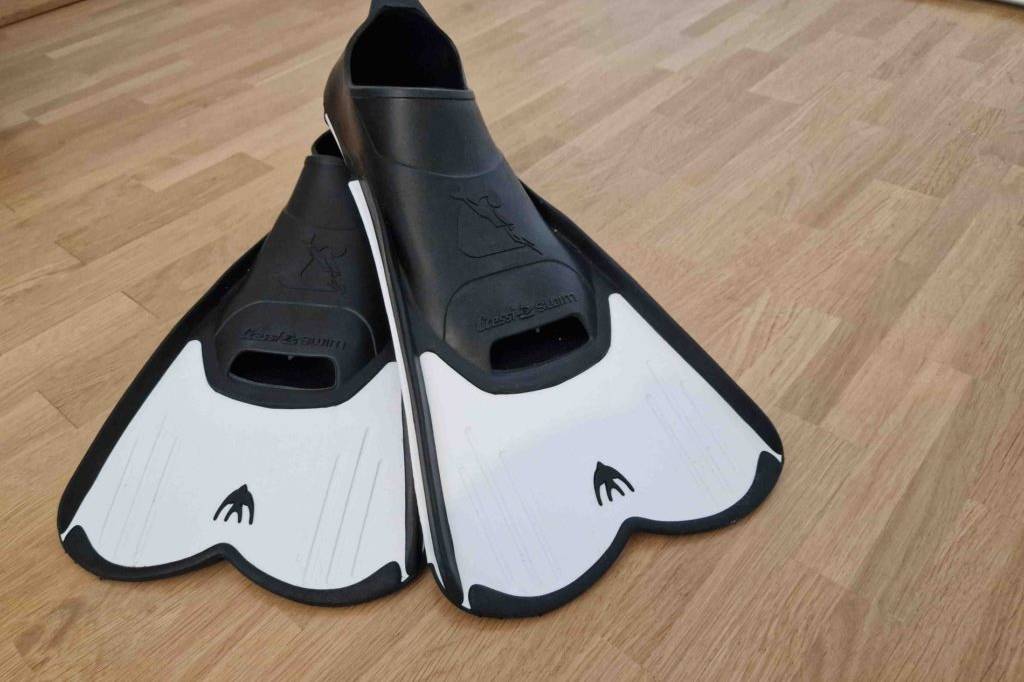 Im Test: Ein Paar schwarz-weiße Kurzflossen von Cressi liegt auf einem Laminatboden.