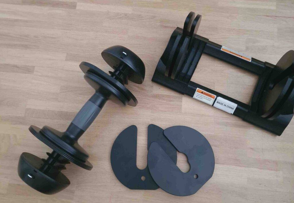 Eine schwarze getestete Kurzhantel mit variierbaren Gewichten liegt neben dem Ständer auf einem Parkett.