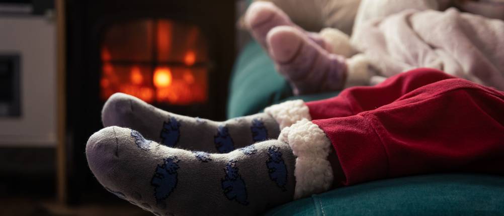 Kuschelsocken-Test: Kinderbeine in roter Hose und Kuschelsocken, Sitz auf Sofa vor Kaminfeuer.